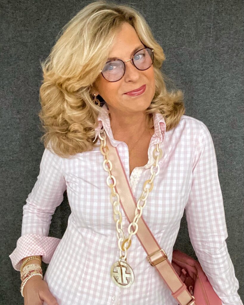 A woman with voluminous honey blonde shoulder-length curls and a deep side part.