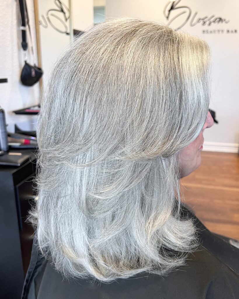 A side profile of a woman with shoulder-length icy silver hair styled in smooth, flowing layers.