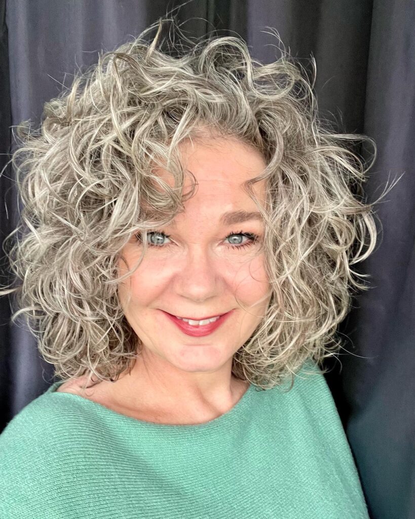 A smiling woman with medium-length curly silver and gray hair styled with high volume and a side part.