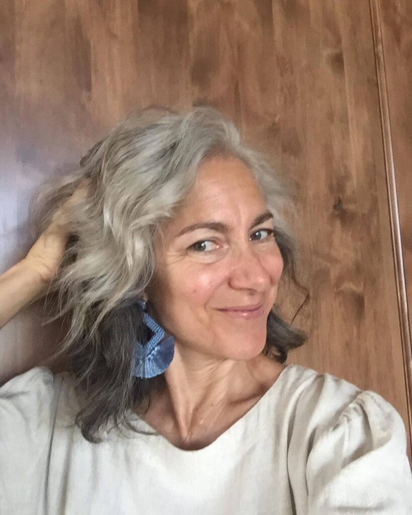 A woman with medium-length salt-and-pepper hair styled in loose natural waves with a side part.