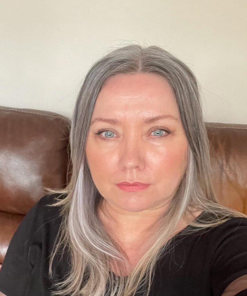 A woman with medium-length straight silver hair featuring bright white highlights and a clean middle part.