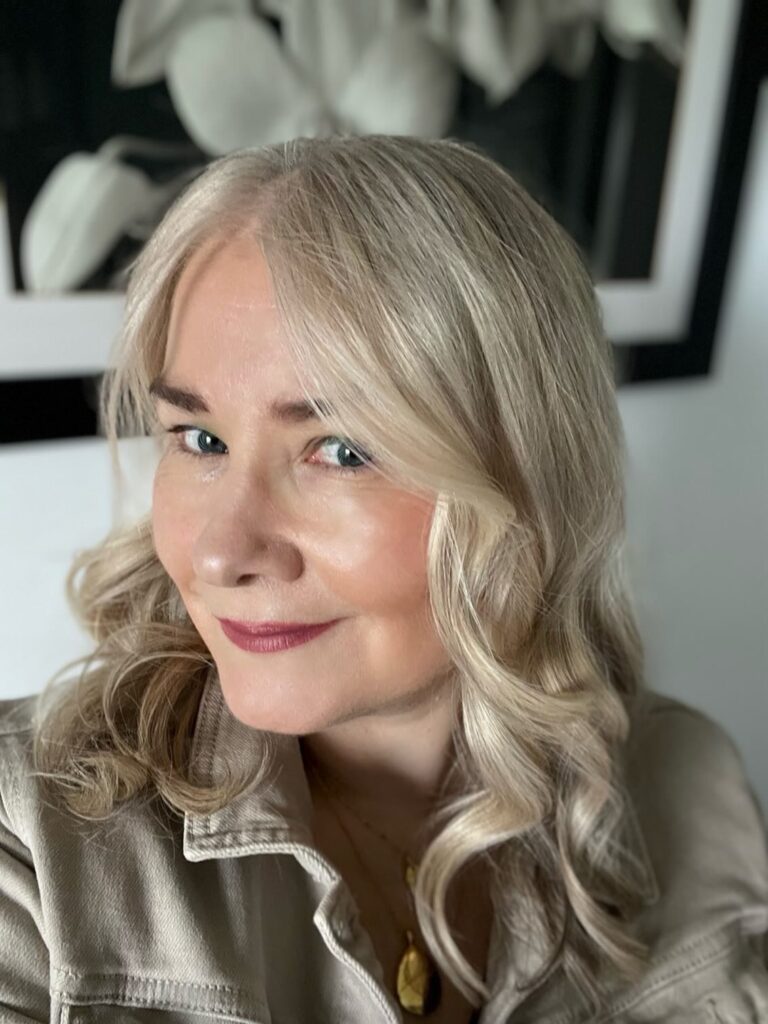 A woman with sandy blonde, medium-length hair styled in soft romantic waves with a side part.