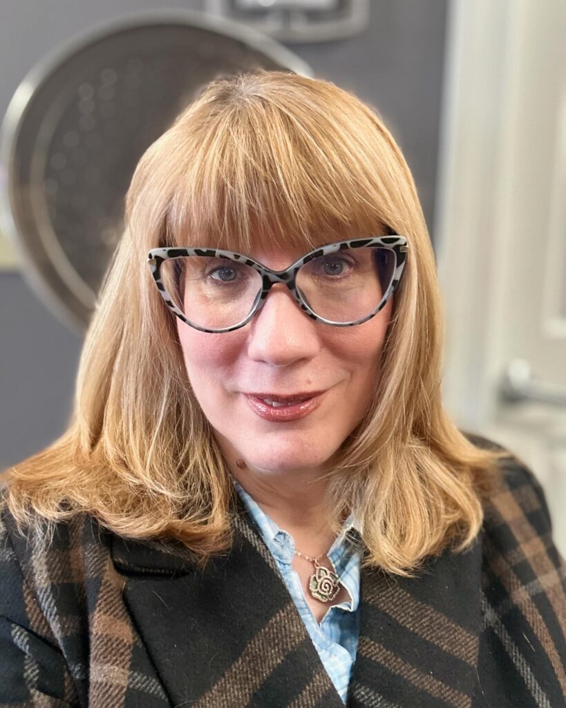 A woman with medium-length strawberry blonde hair featuring light layers and soft bangs.