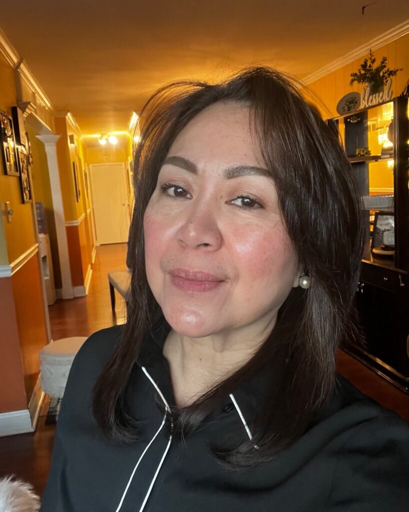 A woman with medium-length straight dark brunette hair styled with soft layers and a gentle inward curve at the ends.