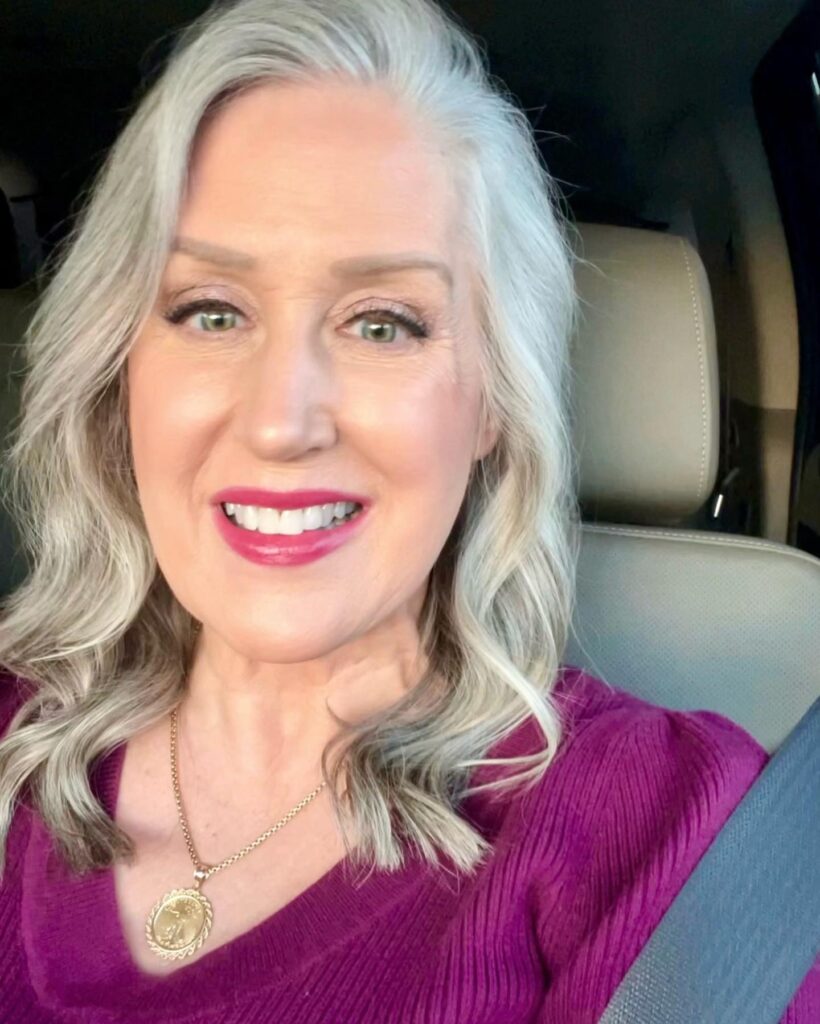 A woman with shoulder-length platinum-silver hair styled in soft beachy waves and a voluminous side sweep.