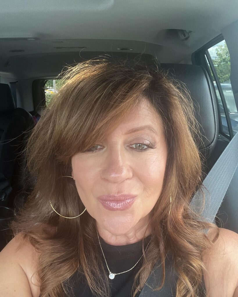 A woman with medium-length warm brunette hair styled in long layers with a side-swept fringe and soft waves.