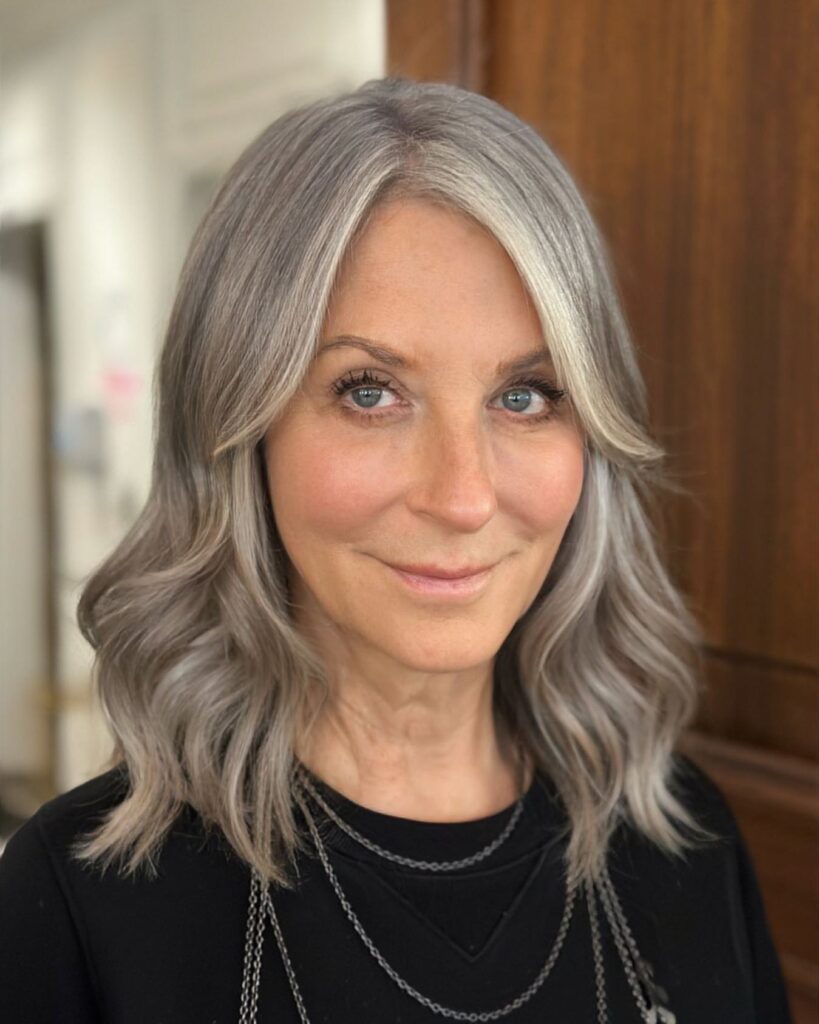 A woman with shoulder-length smoky silver hair styled in soft, textured waves with a center part.