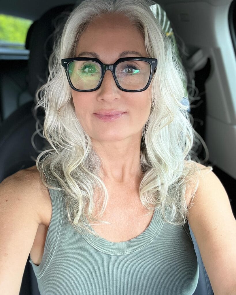 A woman with long silver gray hair styled in soft waves and wearing glasses.