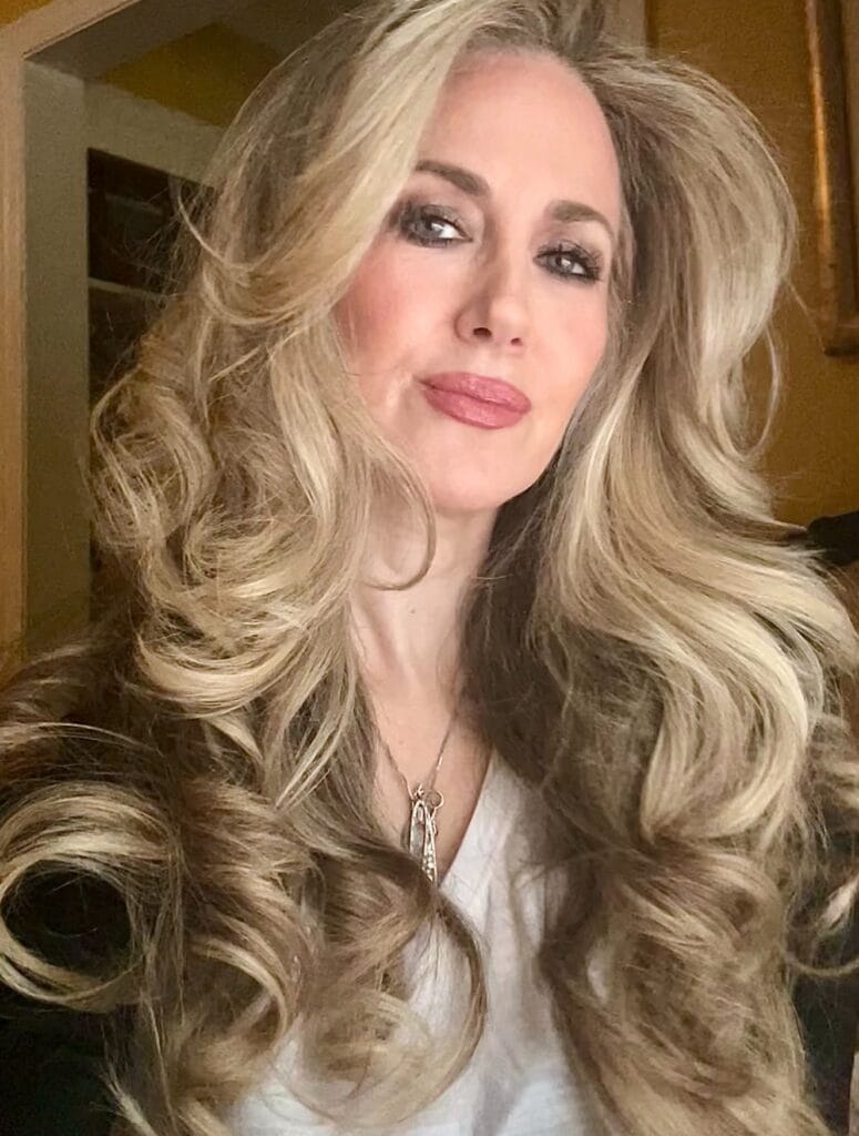 Long layered blonde hairstyle with voluminous soft waves and lifted crown.