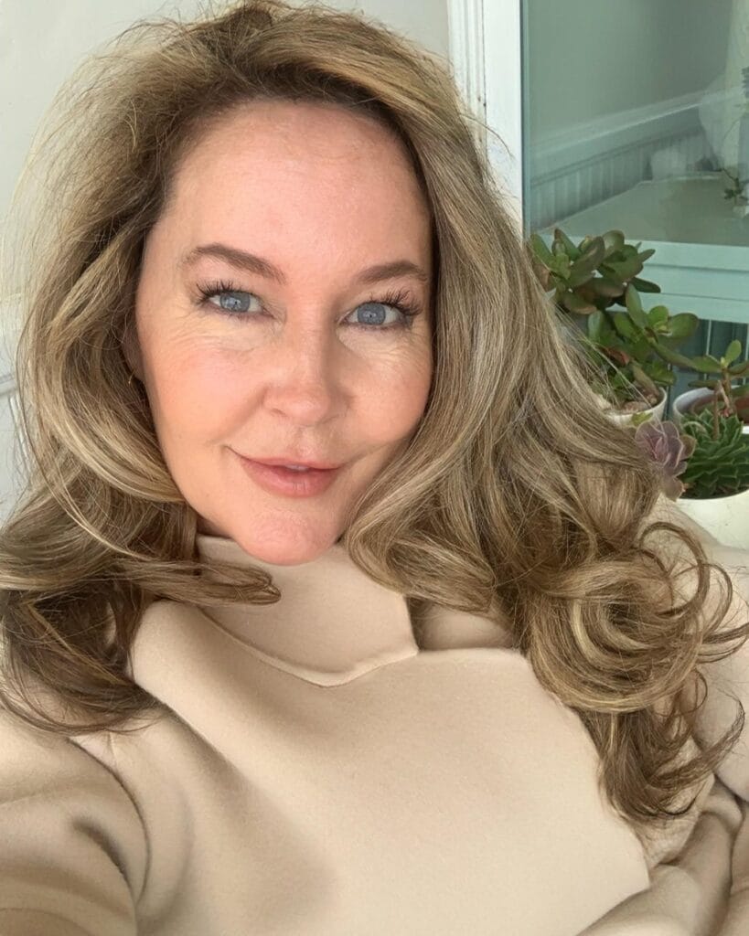 Long layered blonde hairstyle with soft voluminous waves and face framing layers.