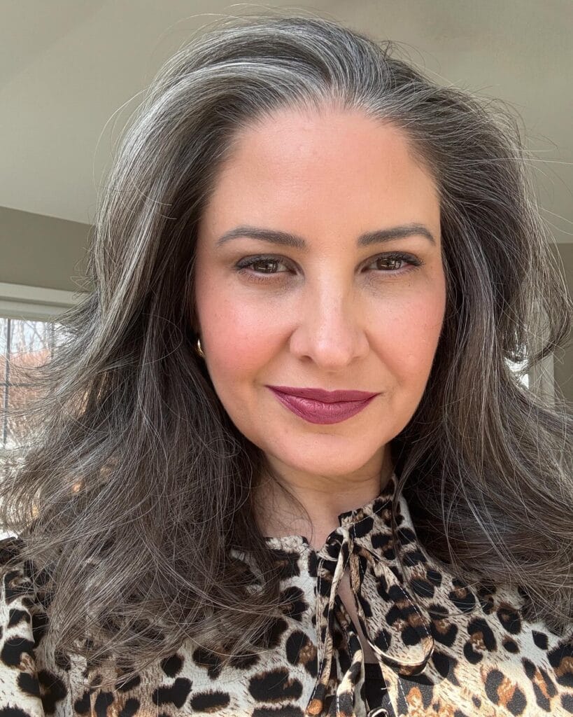 Long layered brunette hairstyle with soft waves and natural gray highlights.