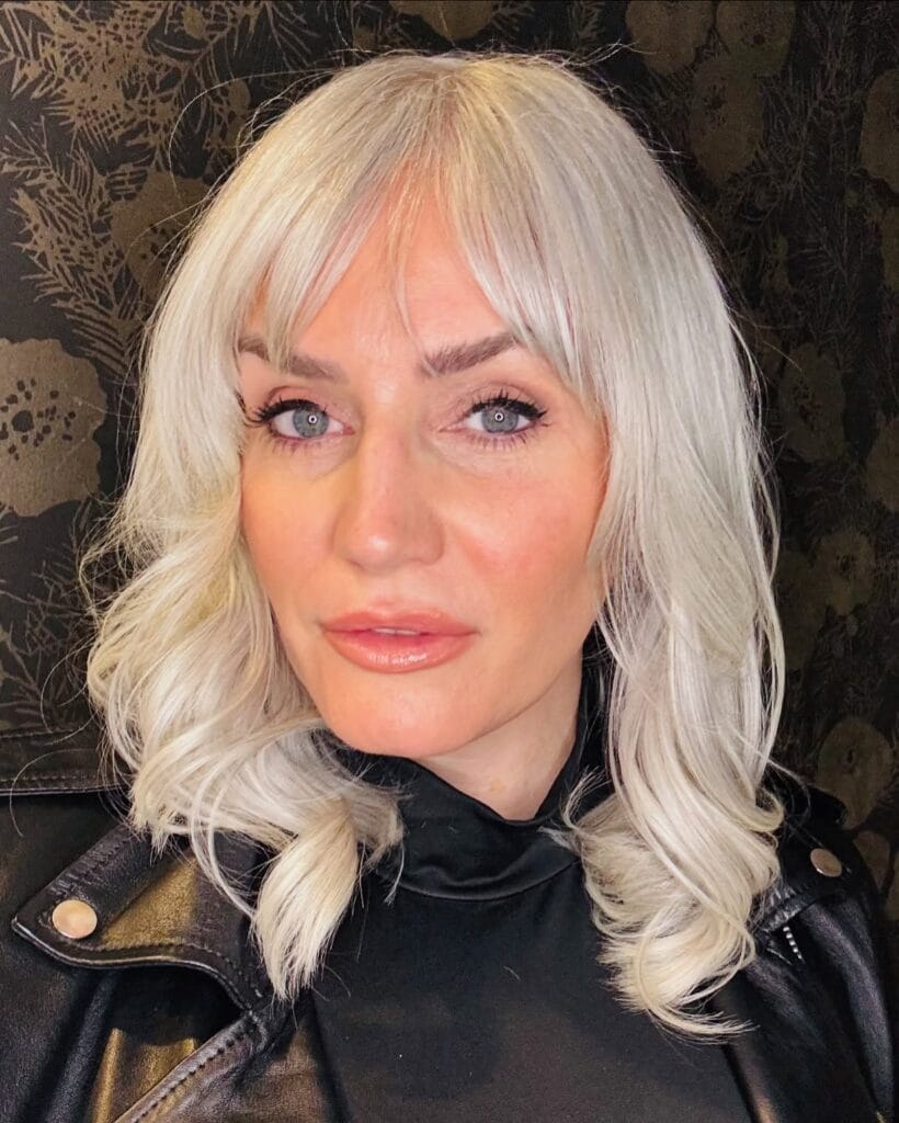 Shoulder length platinum blonde wavy hairstyle with soft curtain bangs.