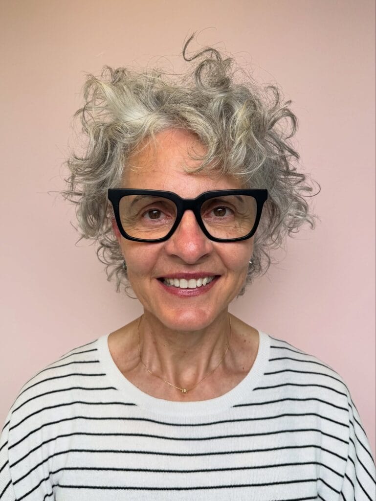 Short gray curly hairstyle with soft volume and a light rounded shape.