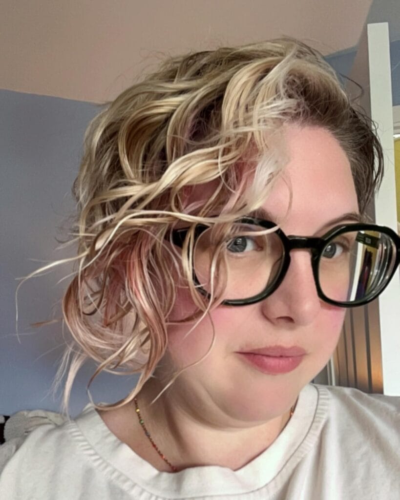 Short tousled blonde wavy bob with loose texture and side swept layers.