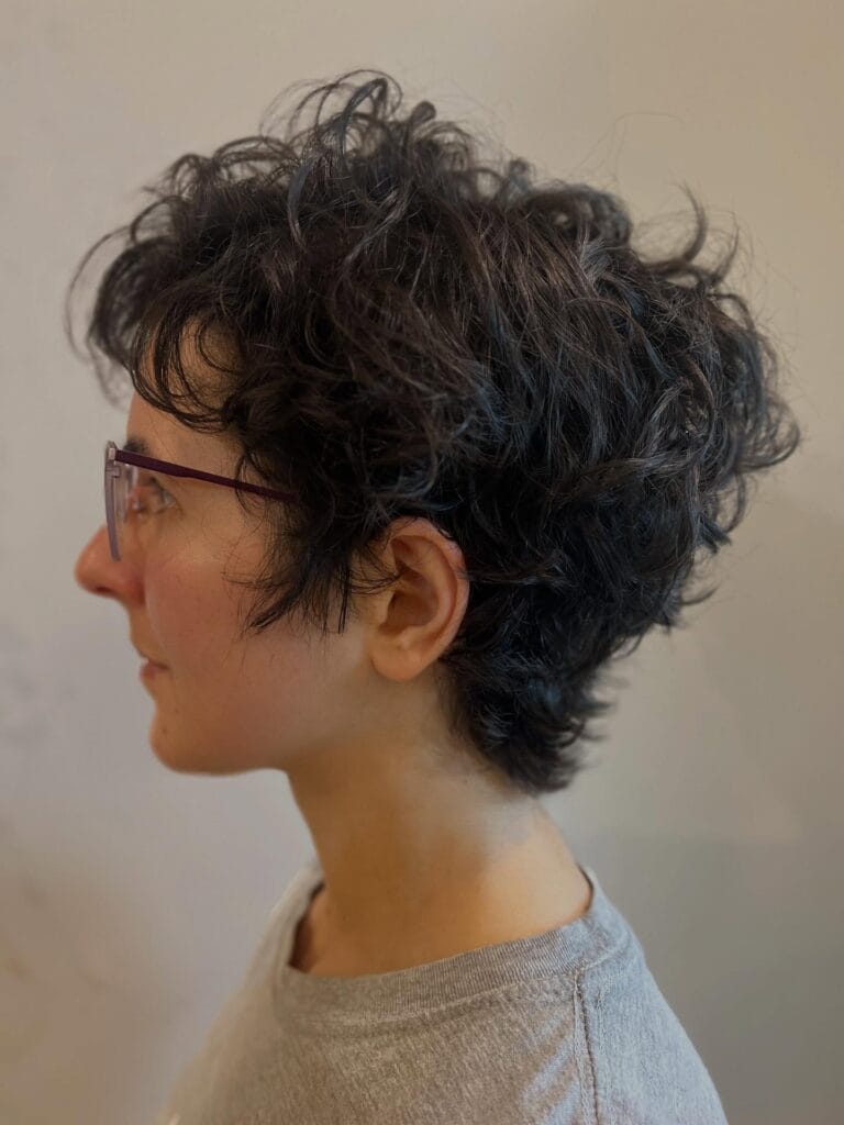 Short dark wavy pixie haircut with textured layers and soft volume around the crown.