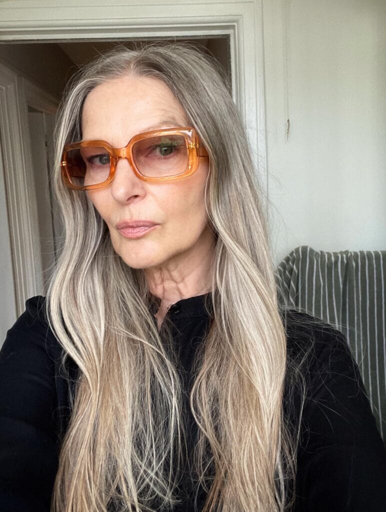 Long silver hair with light layers worn with amber tinted glasses.