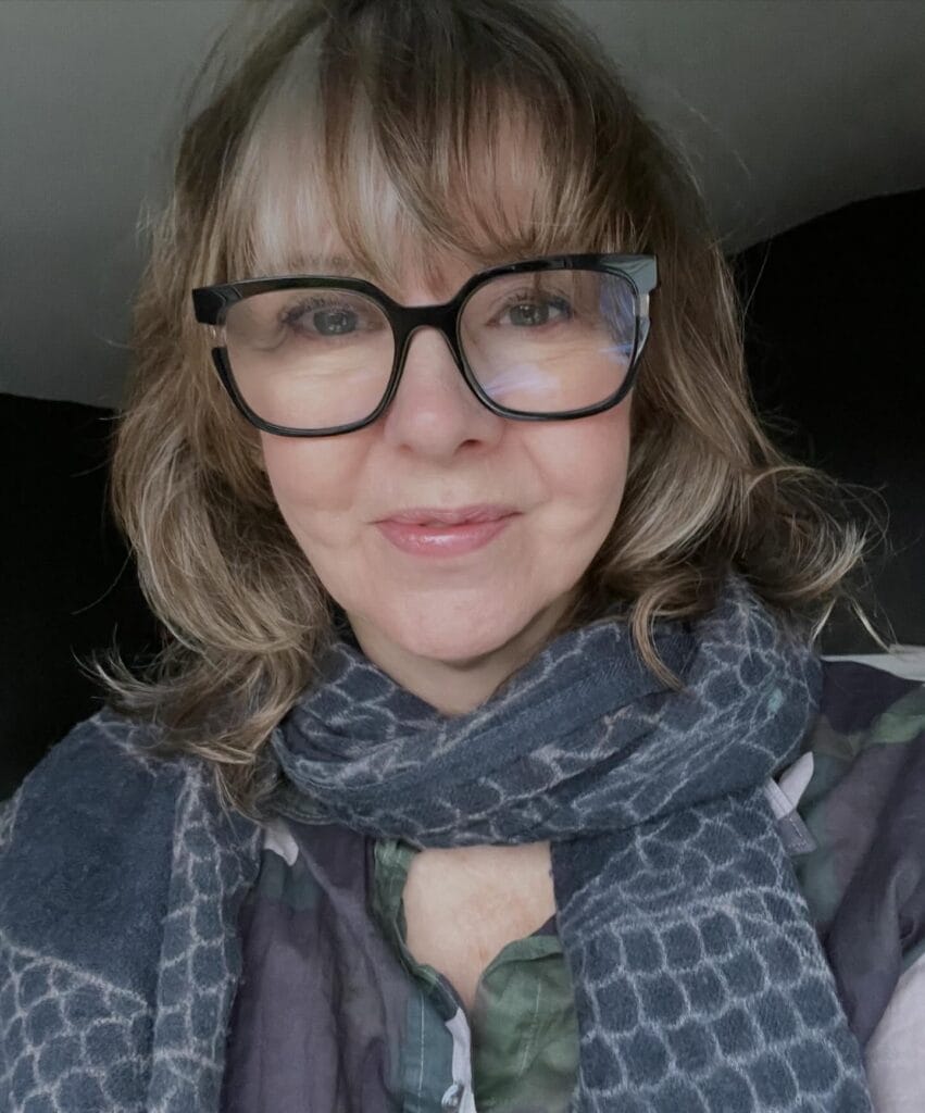 Shoulder length wavy hair with bangs worn with black glasses.