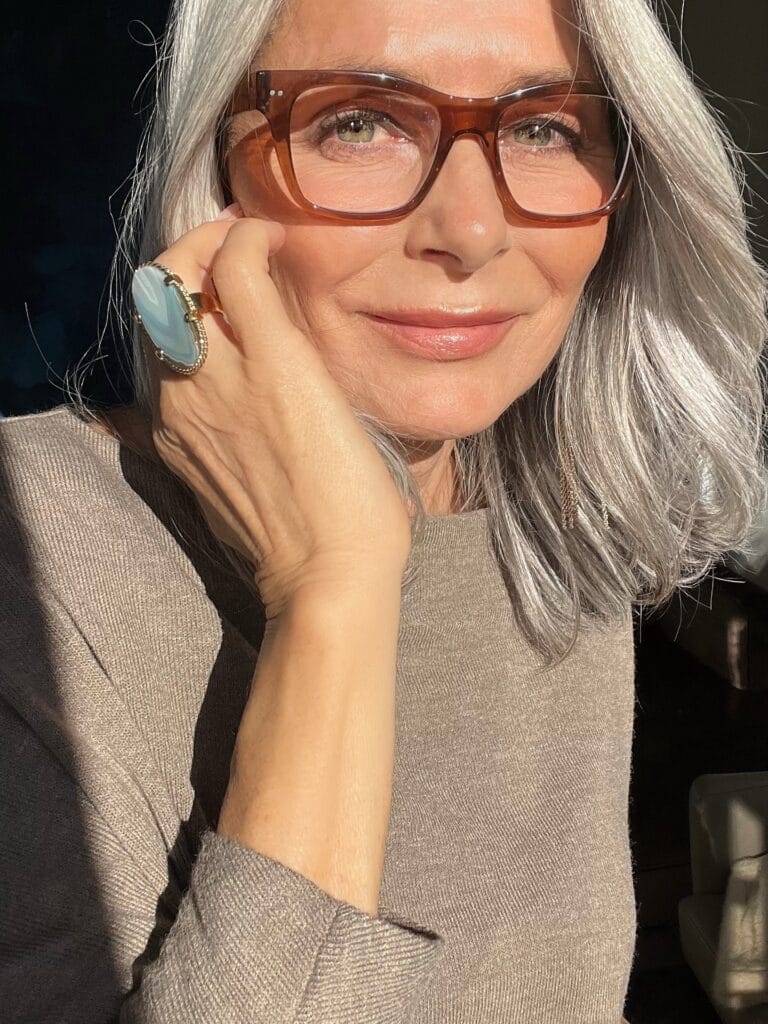 Shoulder length silver wavy hairstyle worn with brown glasses.