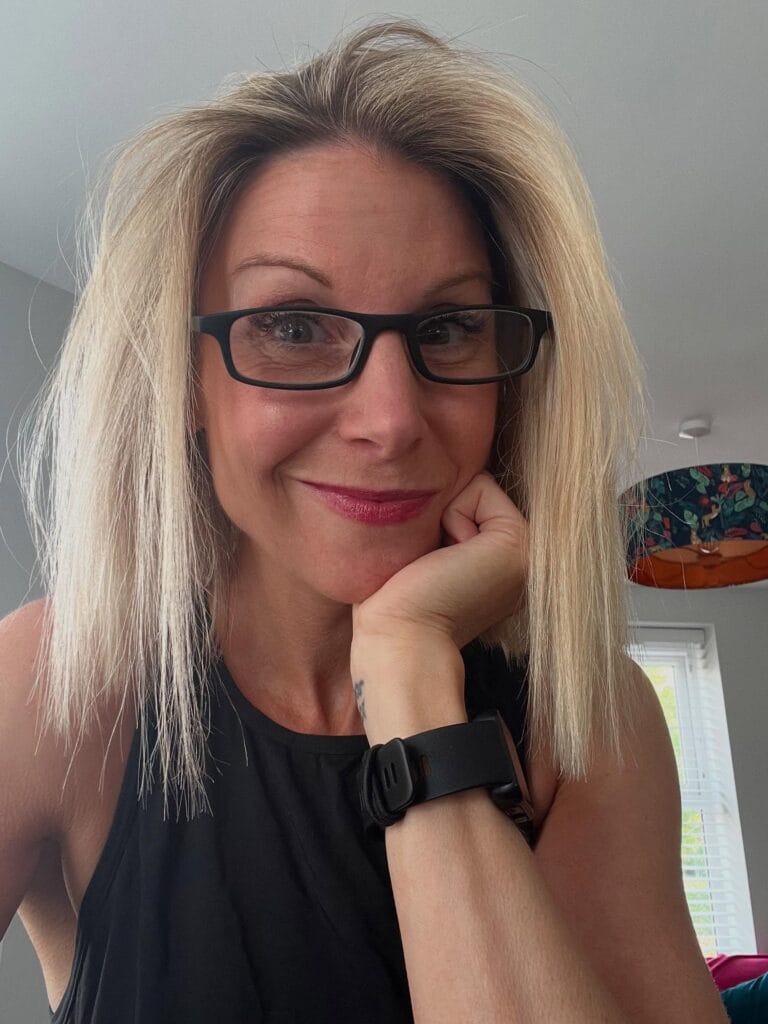 Shoulder length straight blonde haircut with light layers worn with black rectangular glasses.