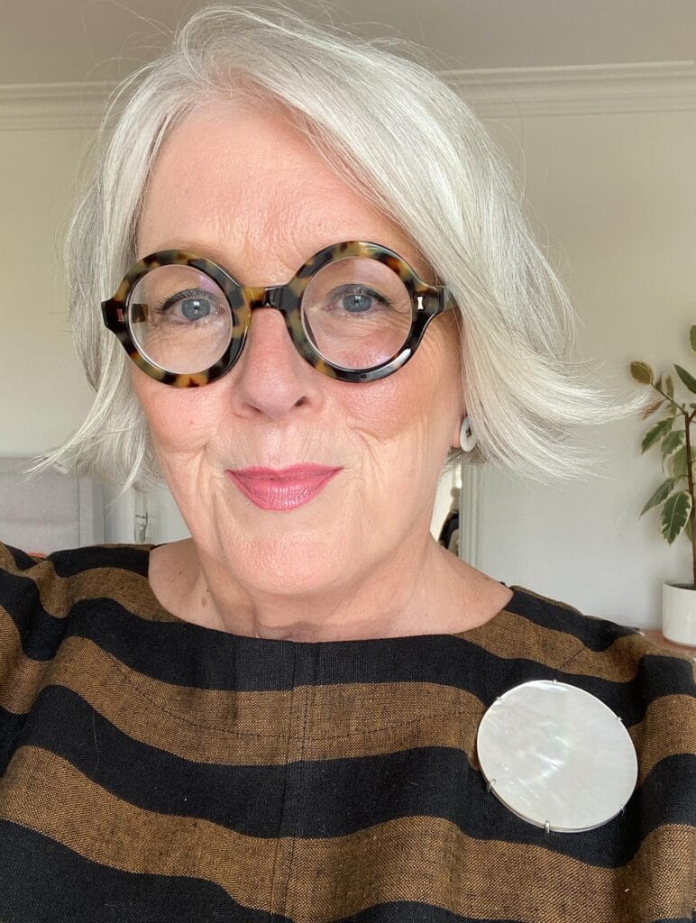 Chin length silver bob hairstyle worn with round patterned glasses.