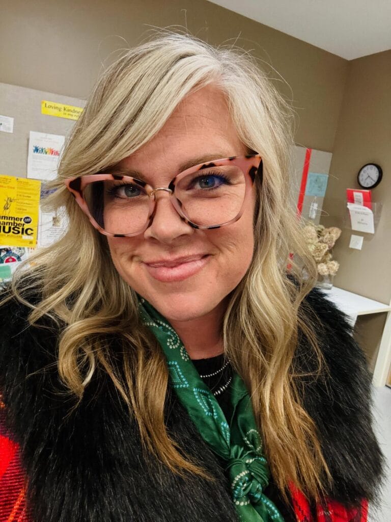 Long layered blonde hair with side swept waves worn with patterned glasses.