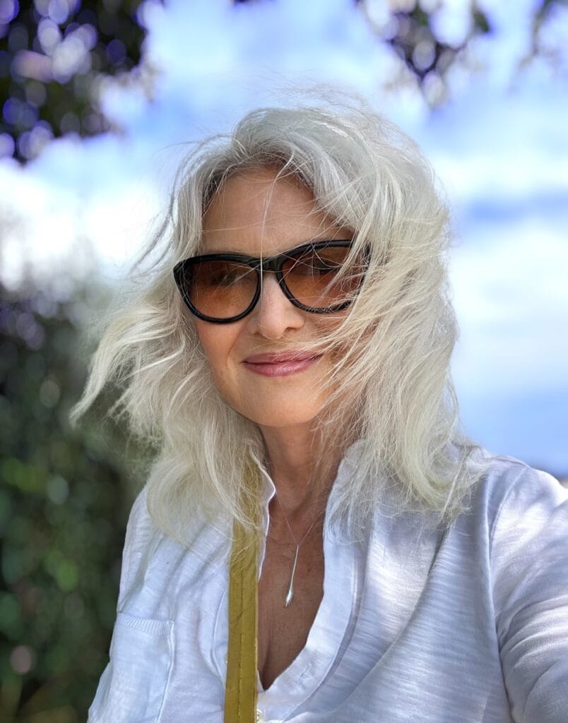 Long silver wavy hairstyle worn with large sunglasses.
