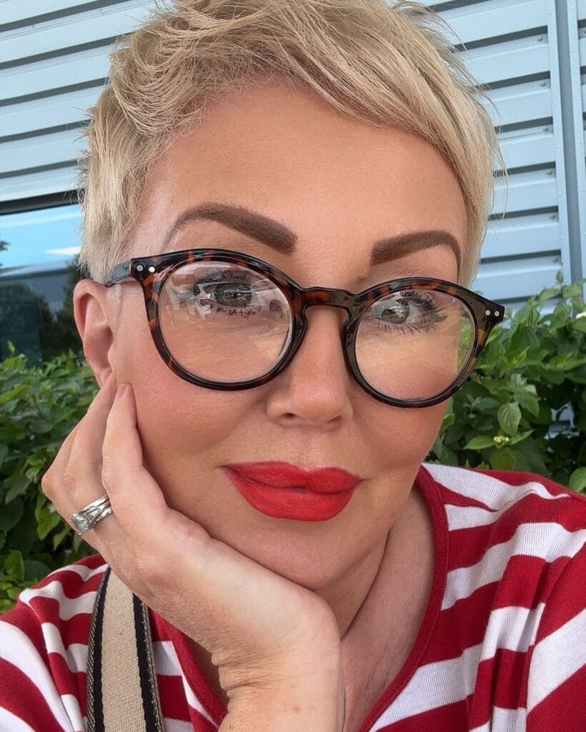 Short blonde pixie haircut with textured layers worn with large round glasses.