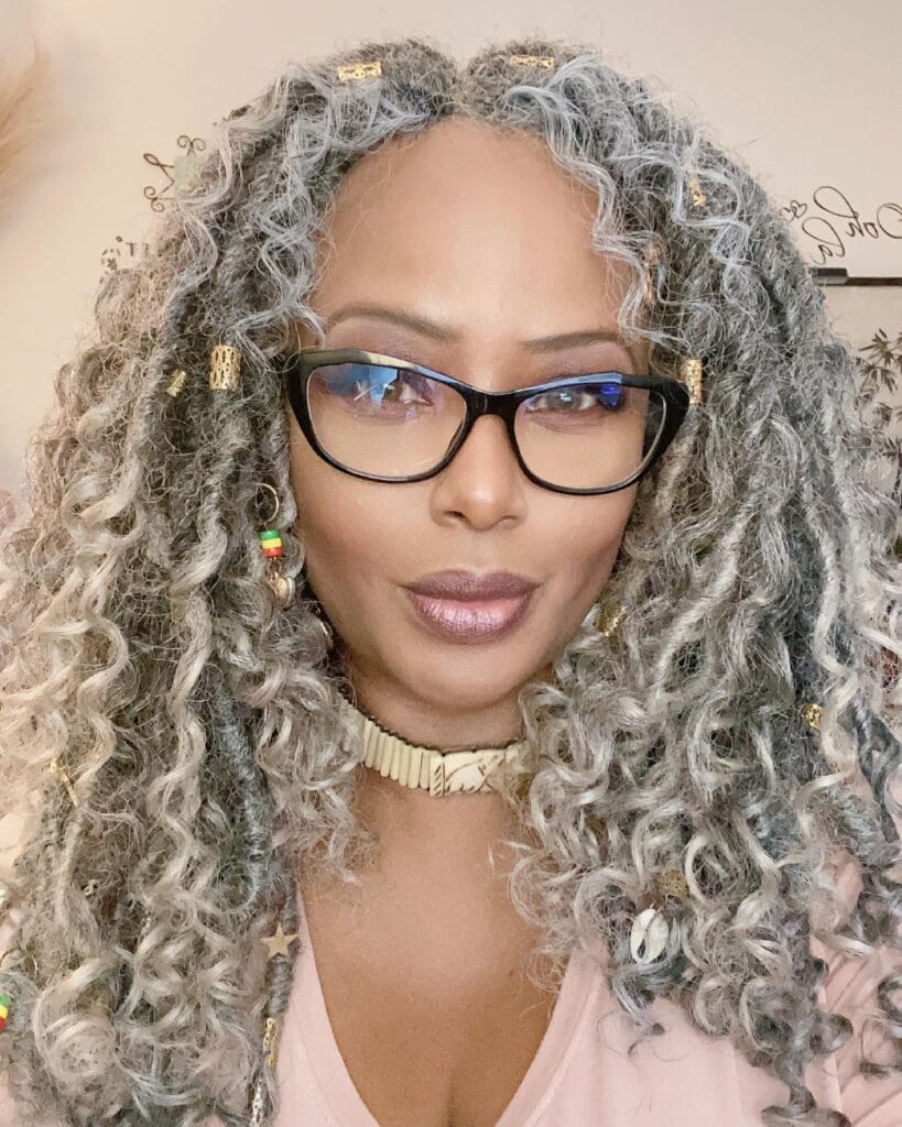 Long silver curly hairstyle with voluminous layered curls worn with black glasses.
