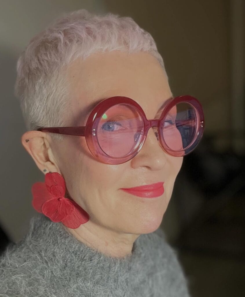 Very short silver buzz haircut worn with oversized pink round glasses.