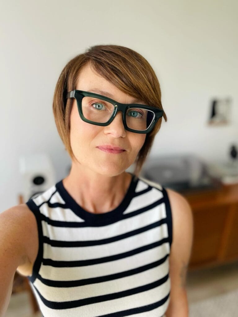 Short side parted bob hairstyle worn with bold green glasses.