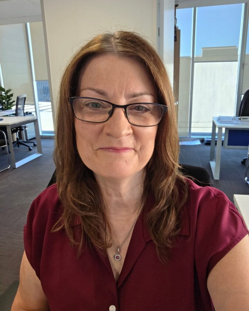 Medium length straight brunette hairstyle with soft layers worn with rectangular glasses.