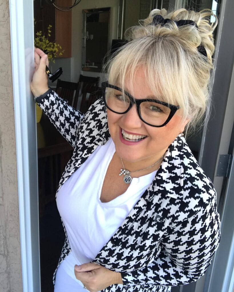 Blonde messy bun with bangs worn with black rectangular glasses.