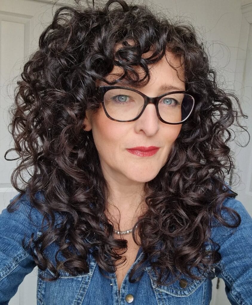 Long dark curly hairstyle with defined curls and voluminous layers.
