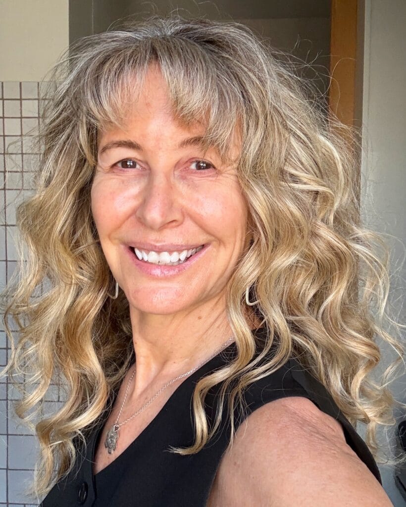 Long curly hairstyle with soft layers and natural blonde tones.