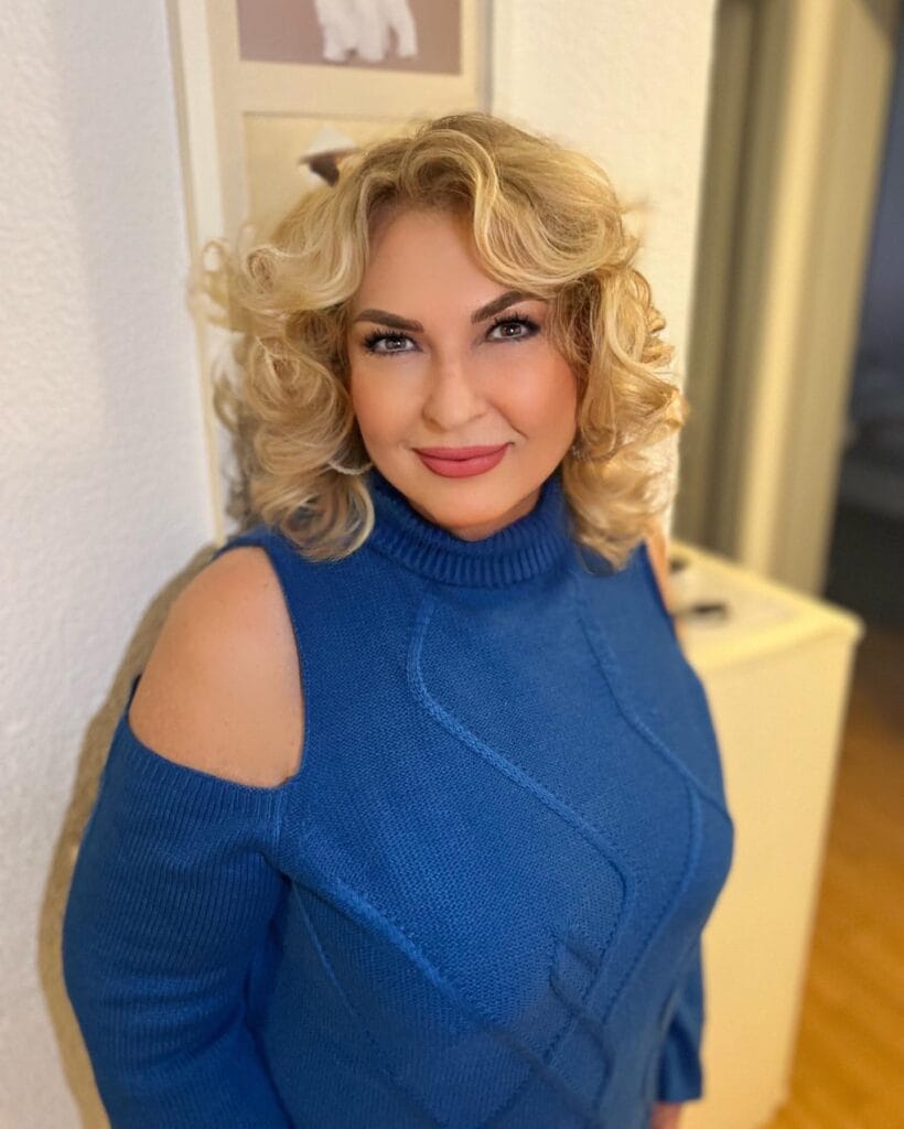 Short curly hairstyle styled into soft voluminous waves with a polished finish.