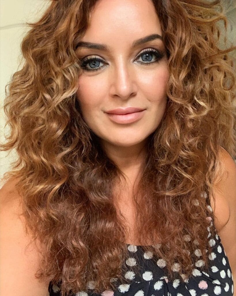 Medium length curly hairstyle with defined curls and copper tones.