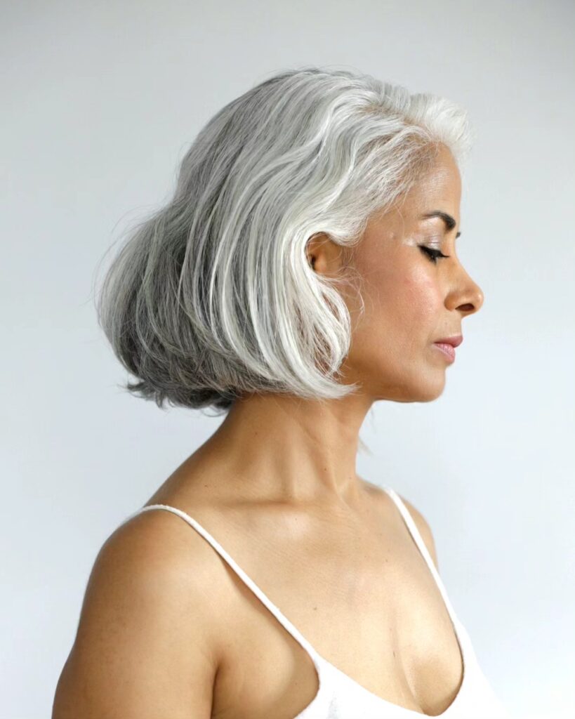 A side profile of a woman with a chin-length silver bob featuring natural waves and a rounded shape.