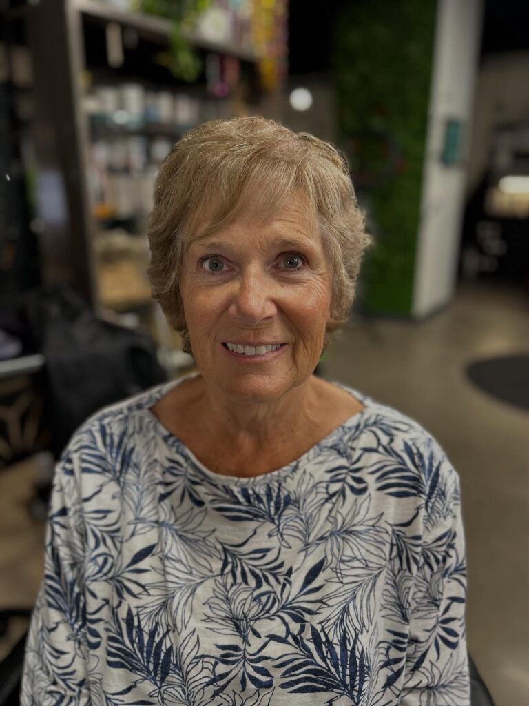A woman over 50 with a short honey-blonde pixie cut featuring soft side-swept bangs and textured layers.