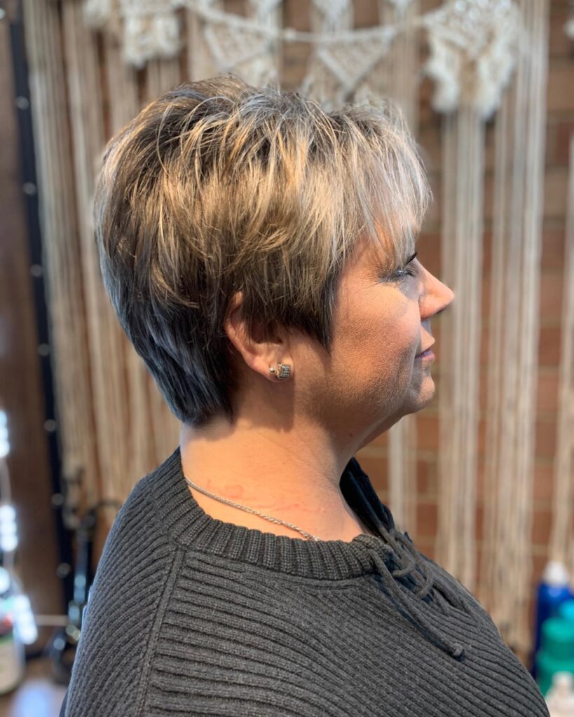 A woman with a short layered pixie cut featuring a blend of blonde and brunette tones with a wispy fringe.