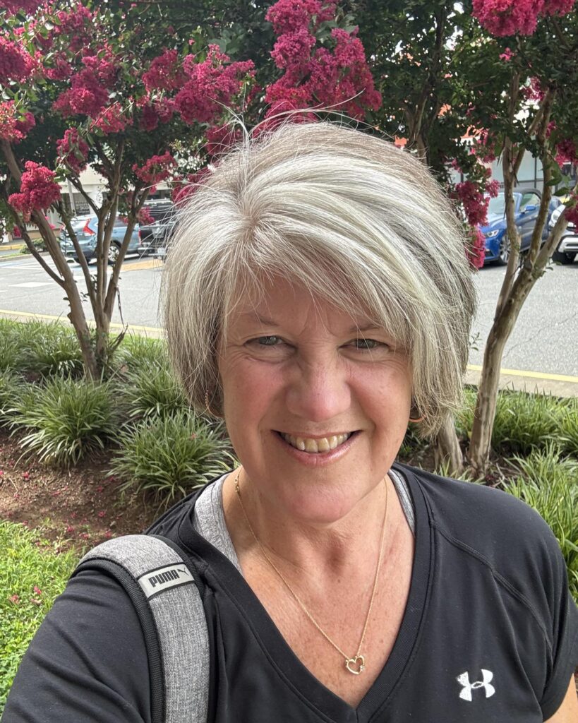 A smiling woman with a salt-and-pepper bixie cut featuring rounded layers and a side-swept fringe.