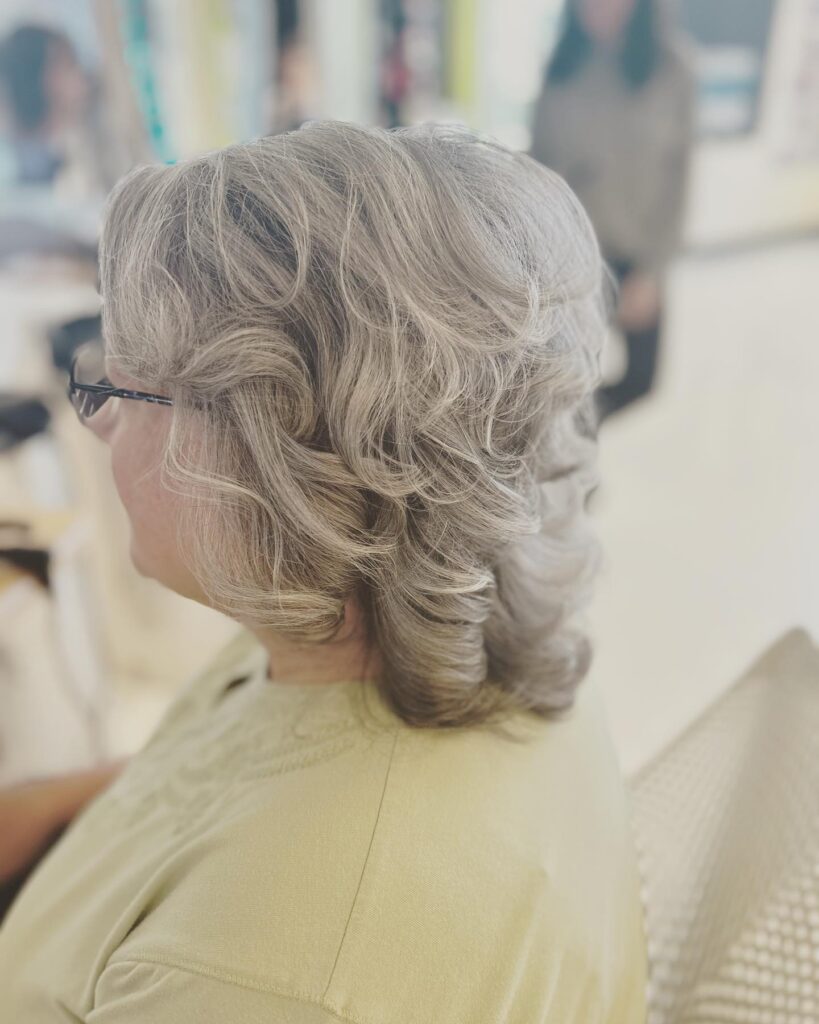 A side view of a woman with a layered silver wavy hairstyle featuring soft curls and elegant volume.