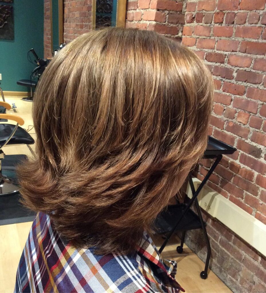 A side view of a woman with a layered caramel brown shag hairstyle featuring flipped-out ends and warm highlights.
