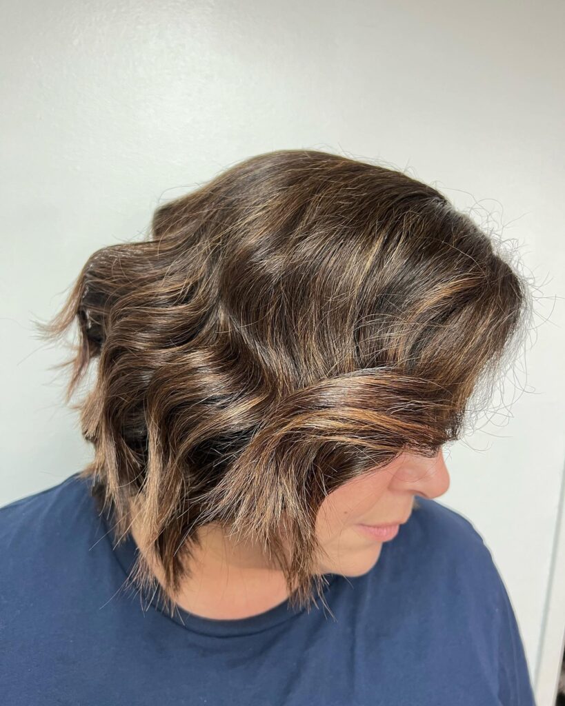 A woman with a neck-length chocolate brown bob featuring relaxed waves and subtle copper highlights.