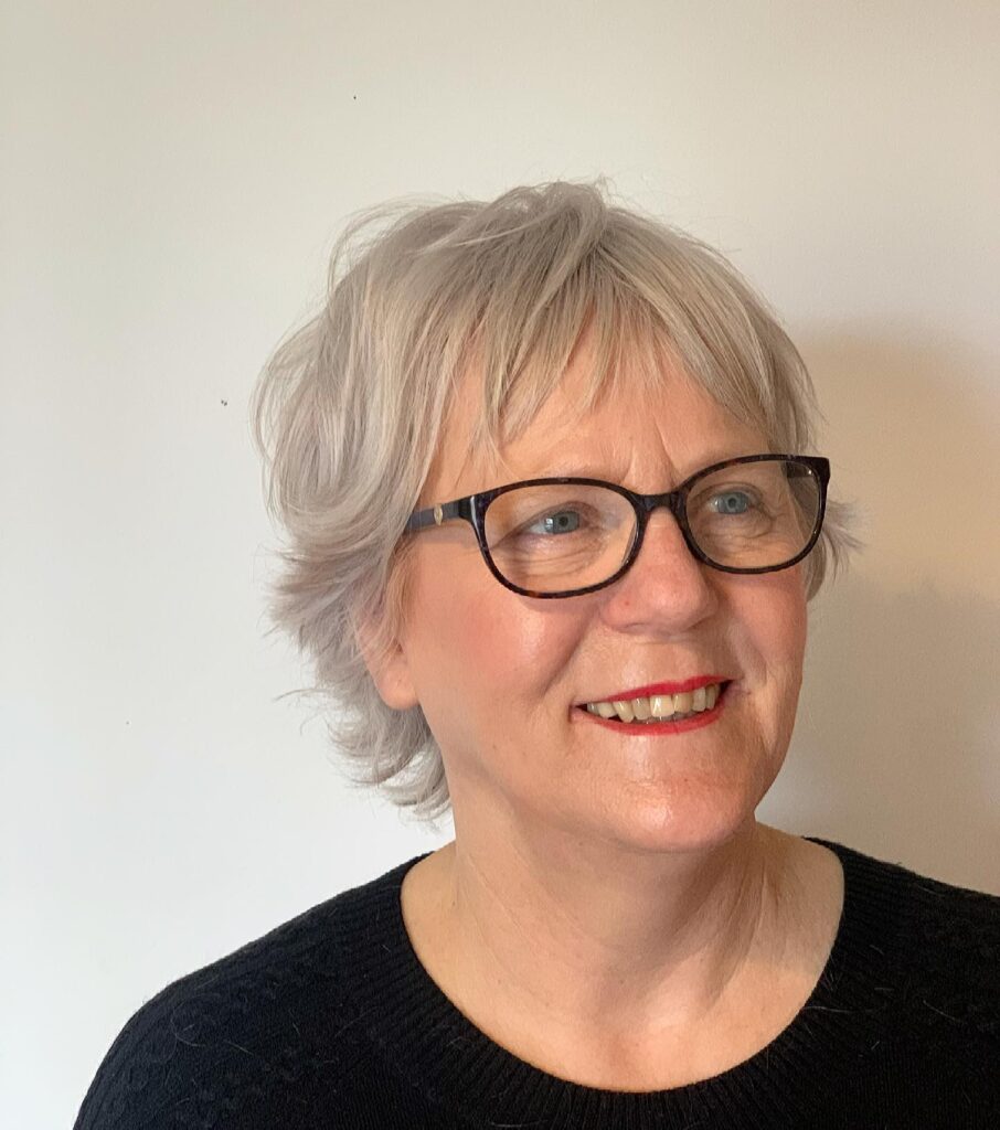 A woman over 50 with glasses wearing a short wispy silver pixie cut with soft layers and fringe.
