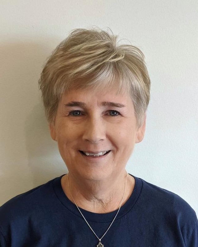 A smiling woman with a soft ash-blonde pixie cut featuring short tapered sides and gentle layers on top.