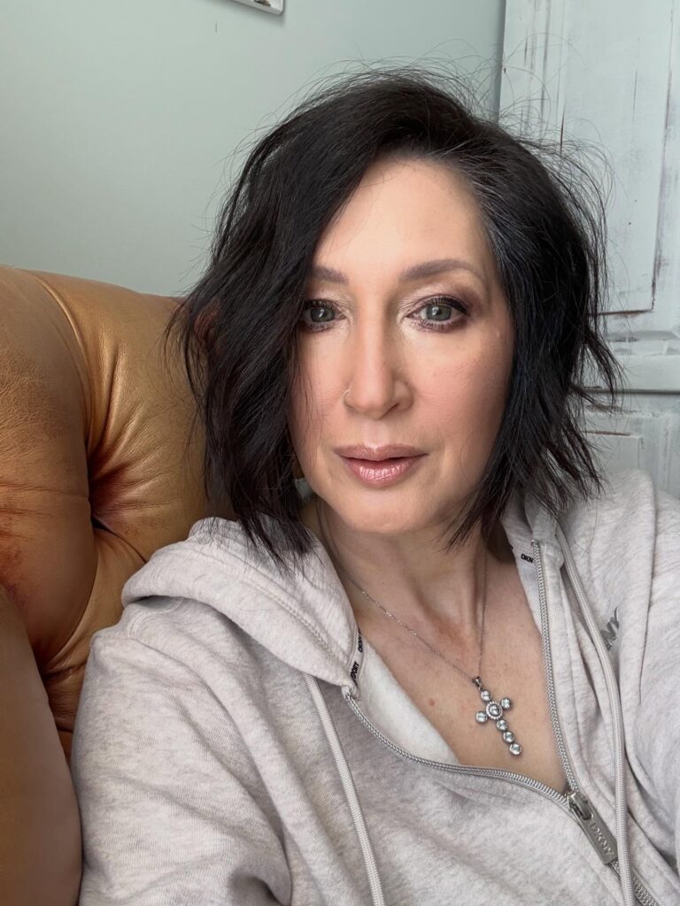 A woman with a choppy espresso brunette chin-length bob and textured layers wearing a gray zip-up hoodie.