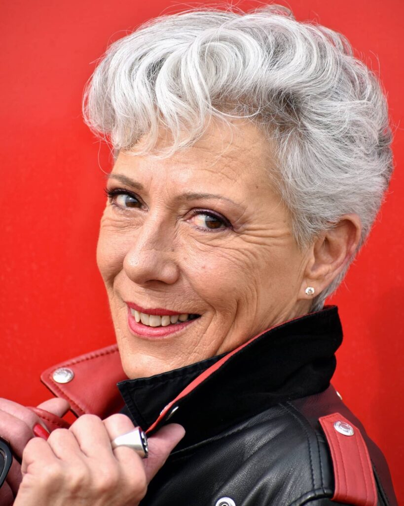 A woman with a textured silver quiff hairstyle featuring finger waves on top and short sides, wearing a black and red leather jacket.