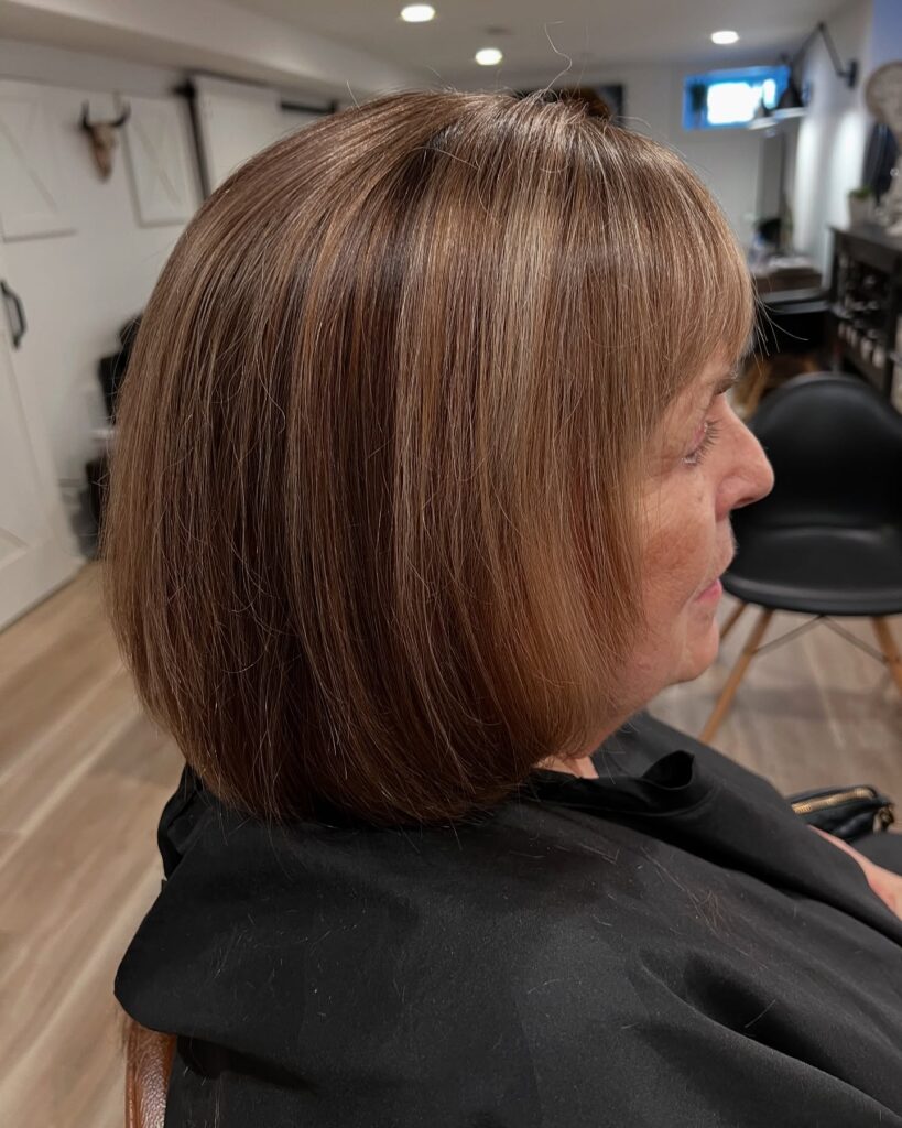 A side profile of a woman with a sleek chestnut brown bob featuring full bangs and subtle highlights.