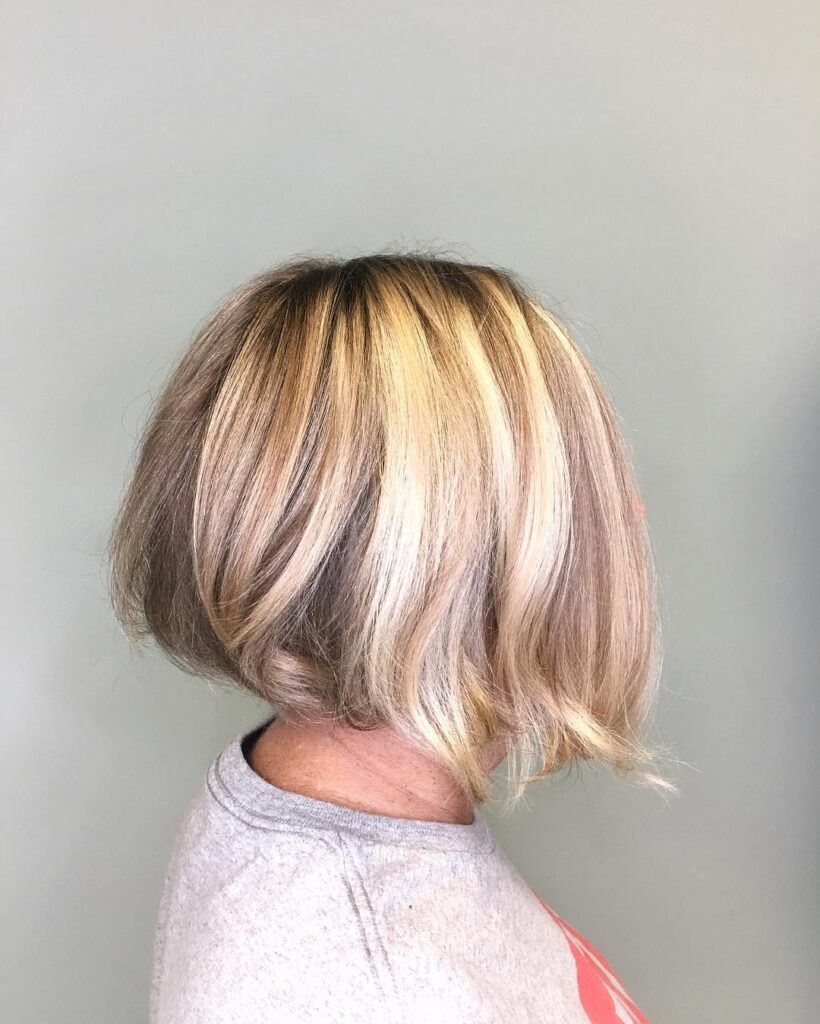 A side profile of a woman with a textured blonde inverted bob featuring an angled cut and dimensional highlights.