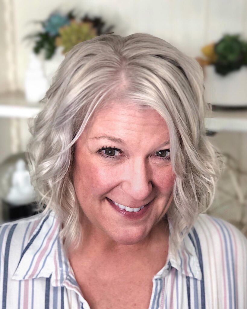 A smiling woman with an icy platinum blonde wavy bob hairstyle wearing a striped button down shirt.